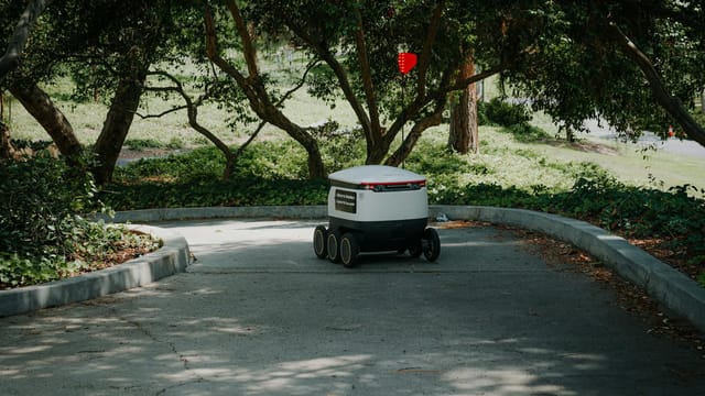 An autonomous delivery robot moves through a shaded pathway in a park, exemplifying modern logistics.