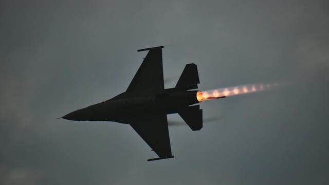 Dynamic F-16 jet showcasing an afterburner flame against a dusky sky.