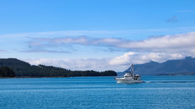 A serene boat sailing across the calm blue waters with a mountainous backdrop under a bright sky.