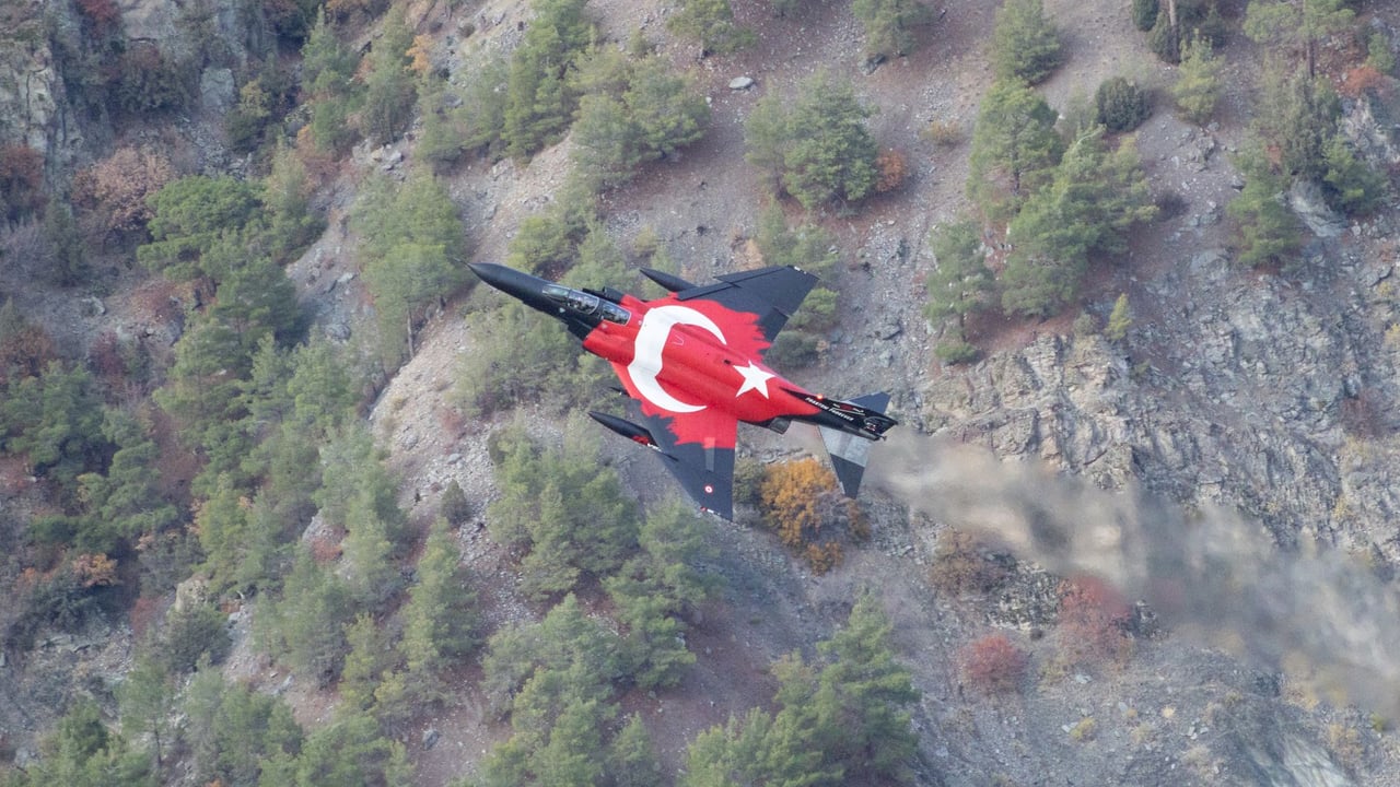A Turkish fighter jet with national colors flies over a mountainous forest area in Eskişehir, Türkiye.