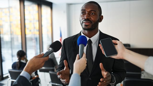 Confident businessman answering questions from the media during a press conference indoors.