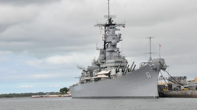 USS Missouri battleship moored at Pearl Harbor in Hawaii under a cloudy sky.