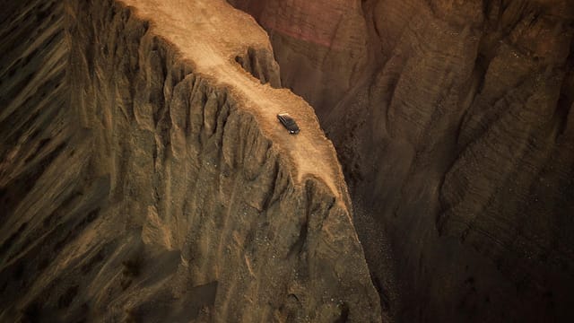 An adventurous aerial shot of a vehicle driving along a dramatic canyon edge in China's Xinjiang region.