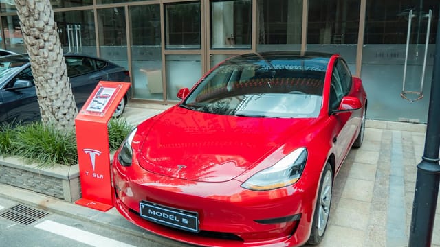 Shiny red Tesla Model 3 parked on sidewalk with reflections on windshield.