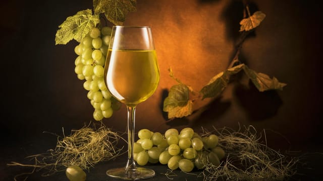 A sophisticated still life of a wine glass with green grapes and vine leaves on a warm, moody backdrop.