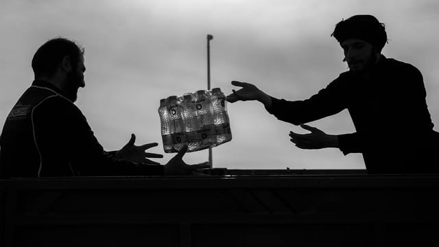Silhouettes of two men exchanging bottled water in Mehran, Iran.