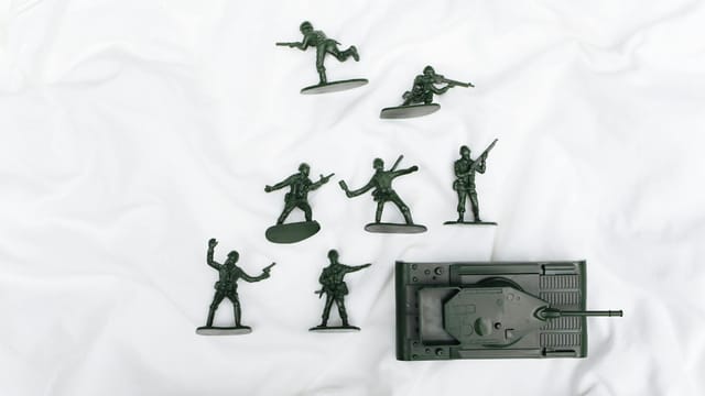 Green plastic toy soldiers and tank arranged on a white backdrop.