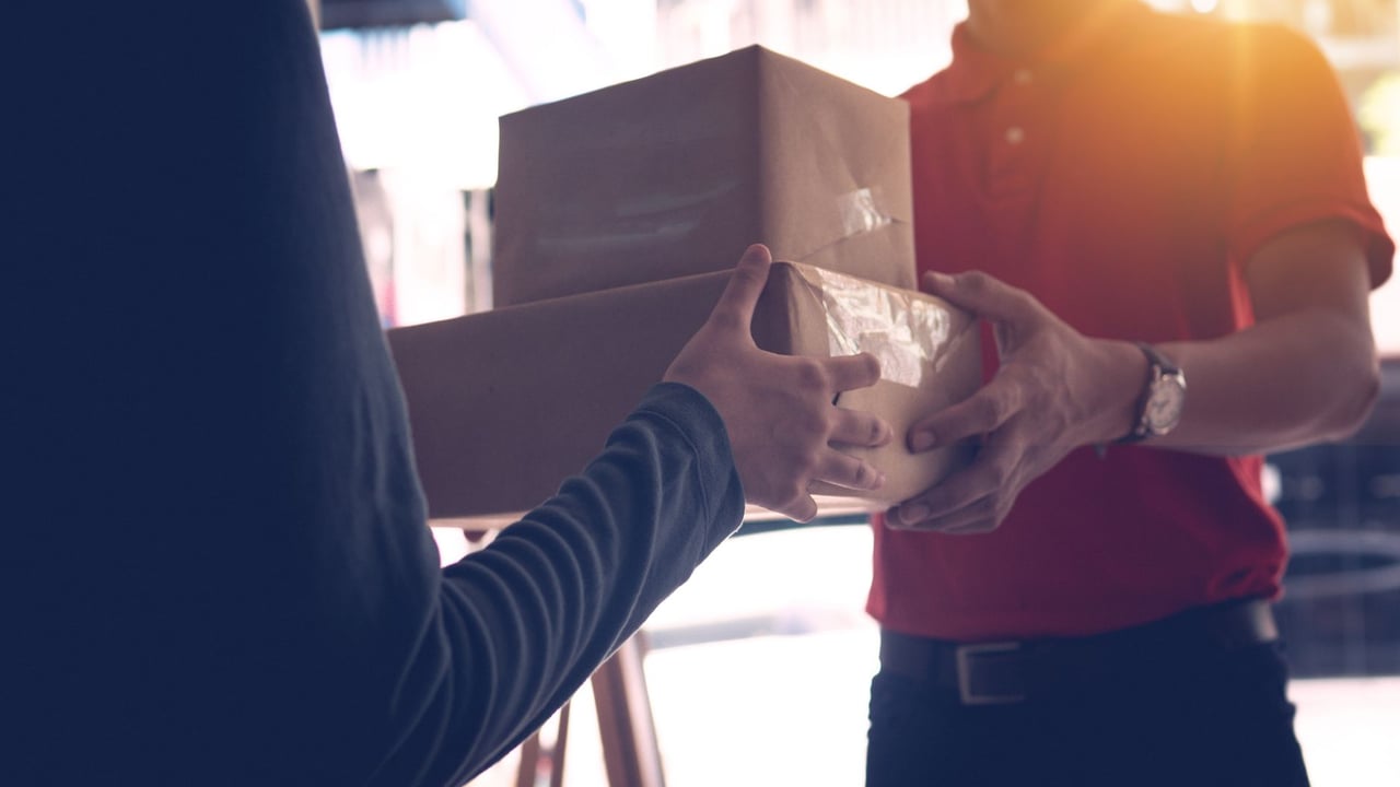 Close-up of a delivery service worker handing over packages to a customer indoors.