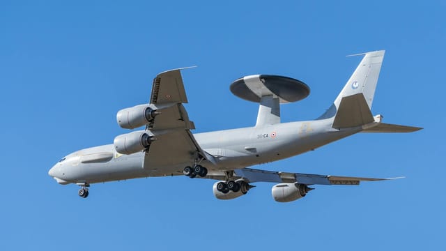 A military aircraft flying against a clear blue sky, showcasing its powerful engines and radar system.