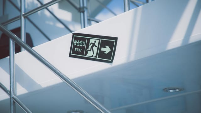 From below of rectangular signboard with EXIT title and symbol of running figure near stairs with handrail in modern house