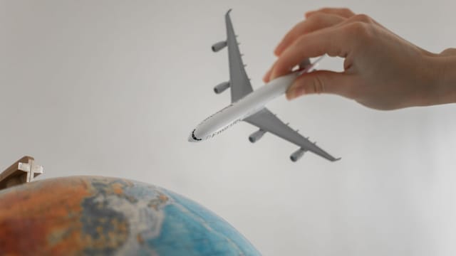 A hand holds a toy airplane above a globe, symbolizing travel and exploration.