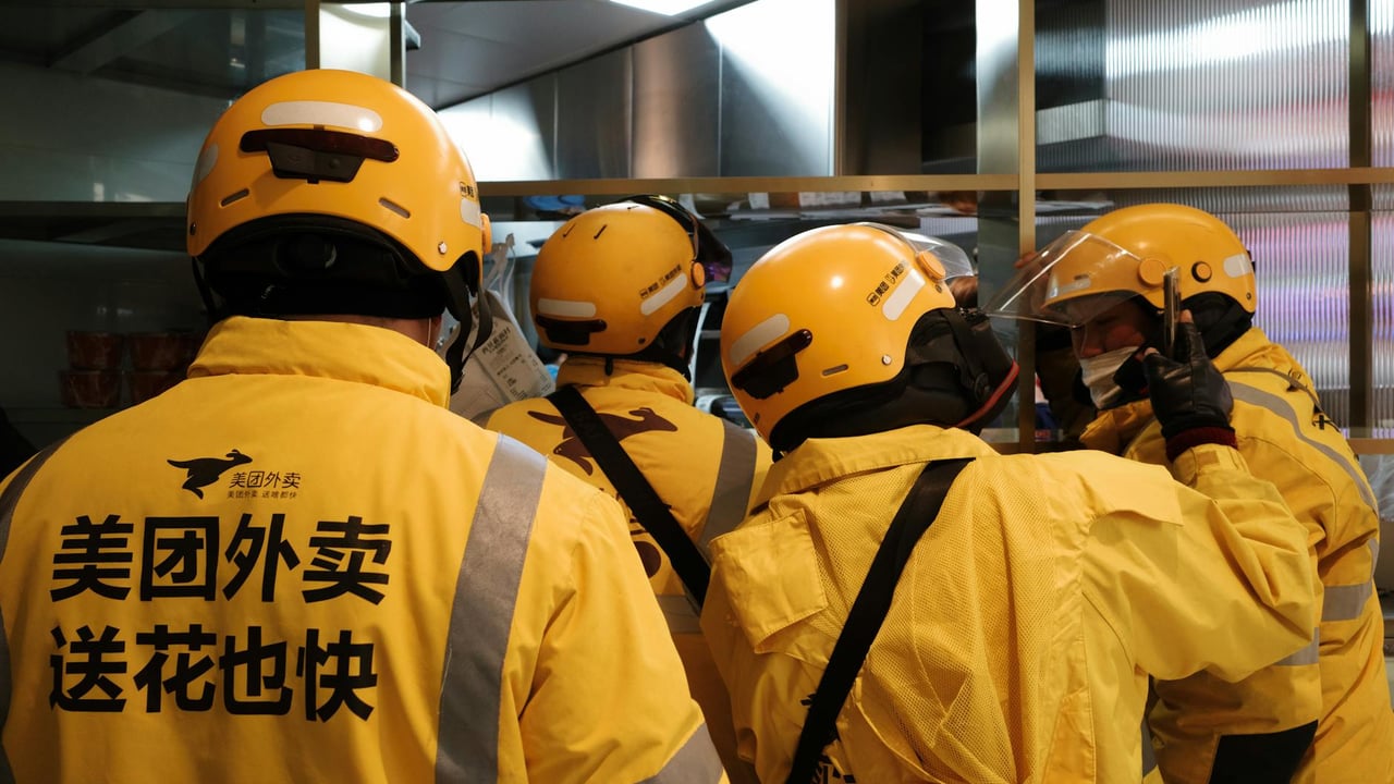 Group of delivery workers wearing yellow uniforms and helmets indoors.