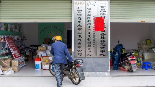 Man pushes motorbike in front of a store in an urban Chinese setting.