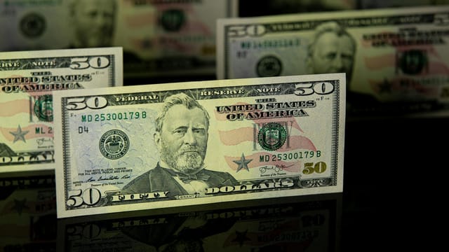Focused shot of fifty dollar bills on a dark reflective surface, highlighting wealth.