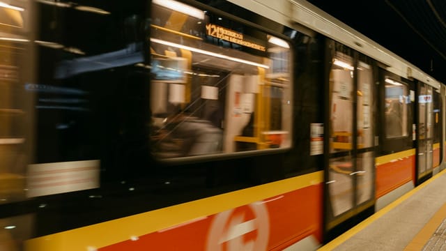 A blurred metro train speeds through an underground station with passengers on board.