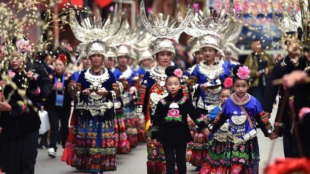 People in traditional Chinese clothing parade during a cultural festival, showcasing vibrant attire and elaborate headpieces.