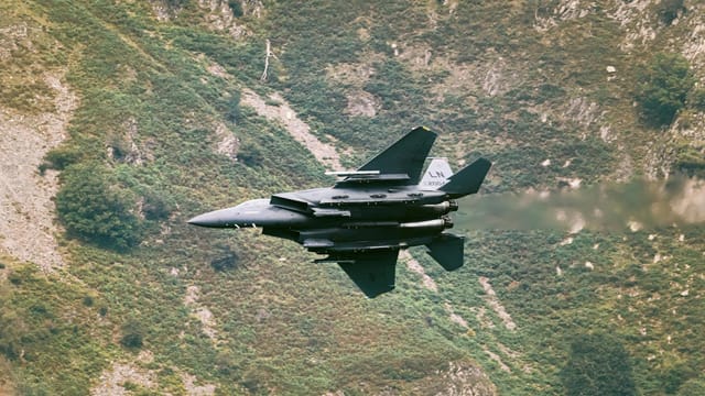 A military jet fighter navigates at high speed across rocky hills, showcasing power and precision.