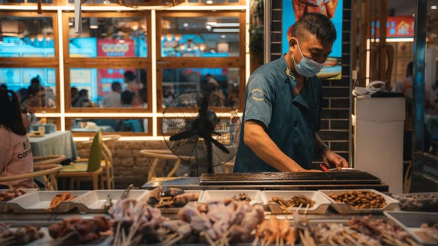 Street vendor in Guilin, China, grilling skewers in a bustling market setting.