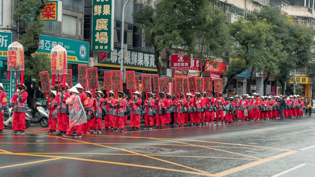 Vibrant parade participants in red traditional attire on a rainy urban street.