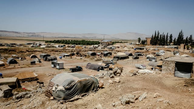 Aerial view of a refugee camp in Idlib, Syria with tents and arid terrain under a clear sky.