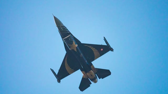 A sleek military jet with striking design flies against a vibrant blue sky, showcasing aerial prowess.