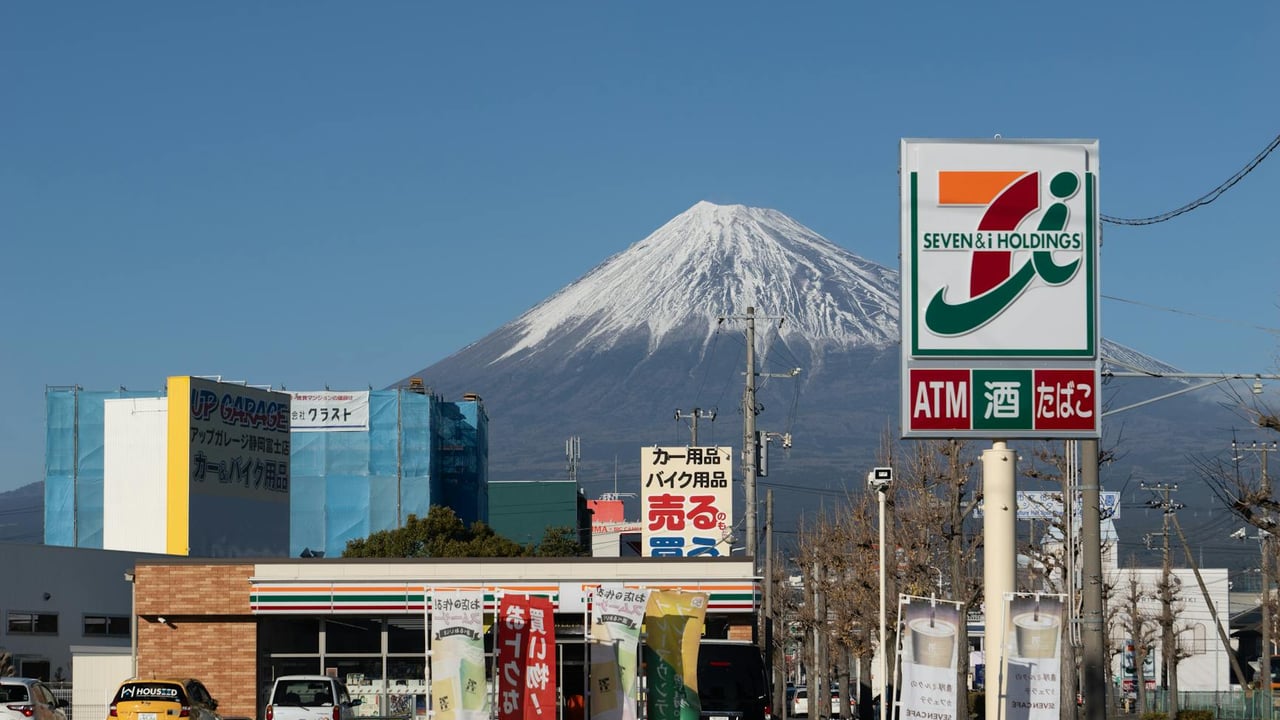 Mount Fuji visible behind a 7-Eleven store sign in Shizuoka, Japan.