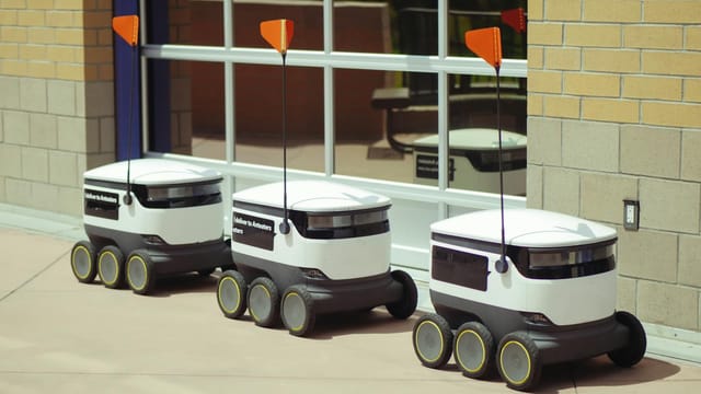 Three autonomous delivery robots parked outside a building, showcasing modern technology.
