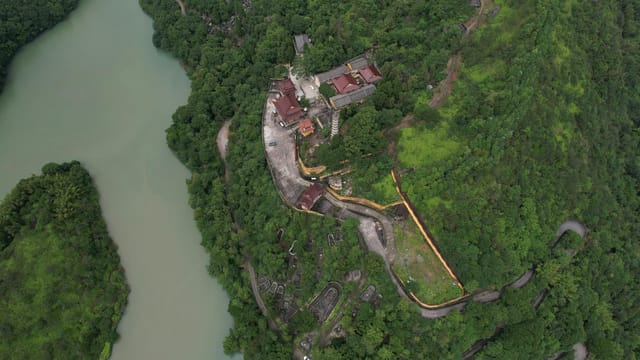 Stunning aerial shot of a temple surrounded by lush green hills and river.