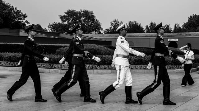 Black and white photo of a ceremonial guard march in Tiananmen Square, Beijing.
