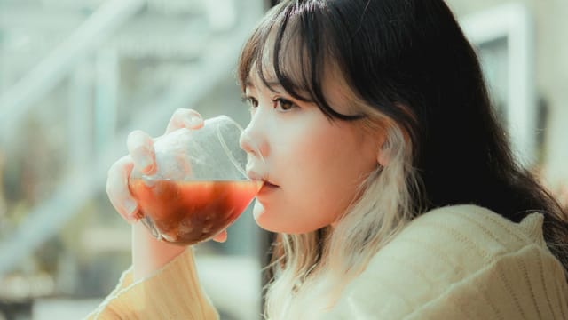 Side view of a woman sipping a refreshing drink indoors on a sunny day.