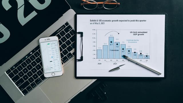 Top view of a financial data analysis setup with laptop, smartphone, and graph on clipboard.