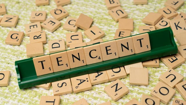 Wooden Scrabble tiles arranged to spell 'Tencent' on a green tile holder, scattered letters in the background.
