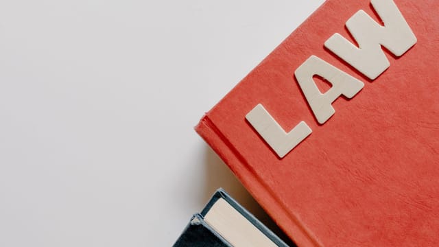 Red law textbook and dark book on white background, symbolizing education.