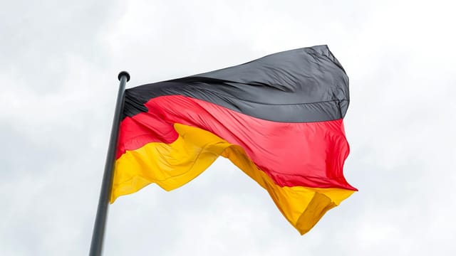 Vibrant German flag flying against a backdrop of a cloudy sky, symbolizing national pride.