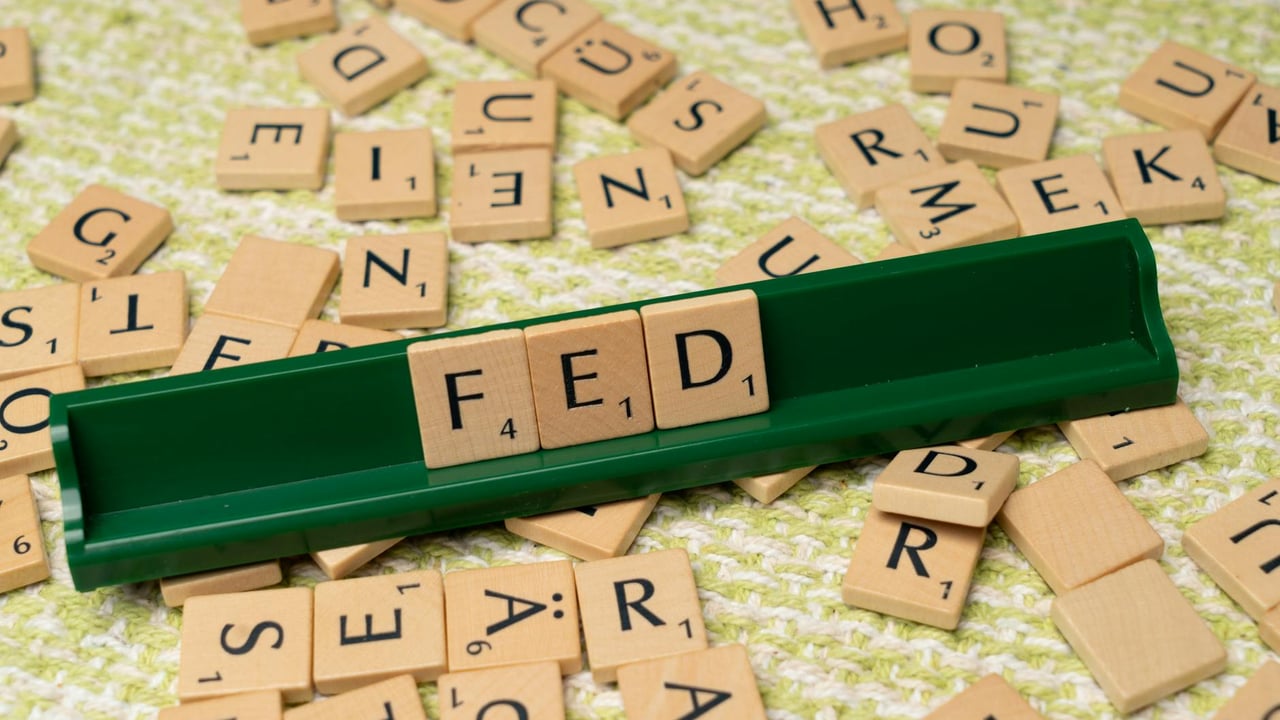 Scrabble tiles spelling 'FED' on a green rack surrounded by scattered tiles on a textured surface.