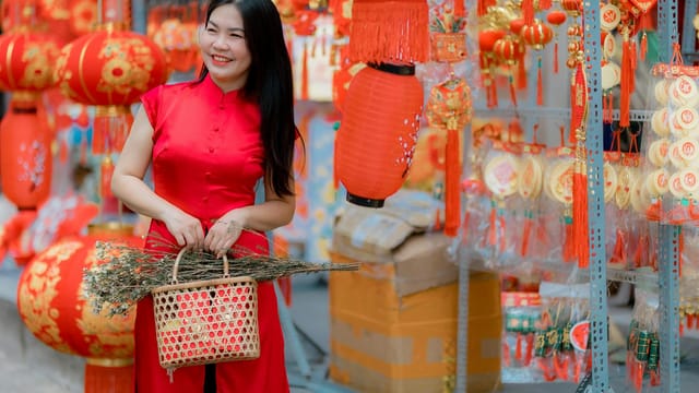 Smiling woman in red dress holds basket among Chinese New Year decorations.
