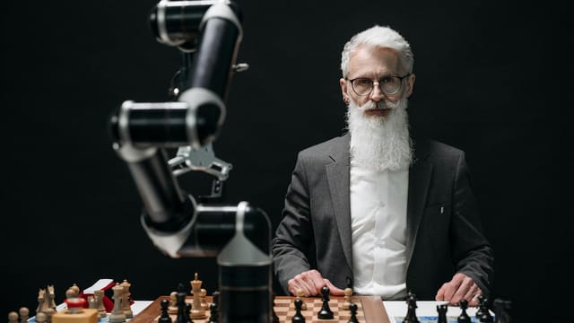 Elderly man in suit competes against a robotic arm in an intense chess game.