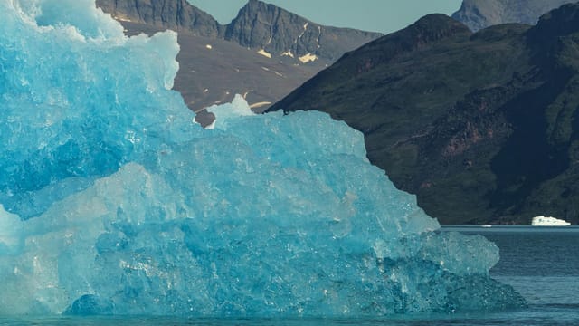 A striking iceberg floats in a calm sea against a backdrop of rugged mountains, capturing the serene beauty of the Arctic.