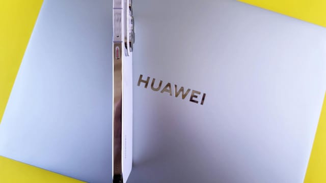 Side view of a smartphone placed on a laptop featuring the Huawei logo on a vibrant yellow background.