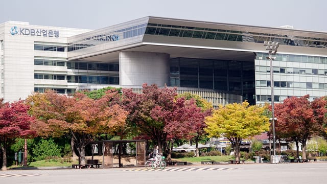 A modern urban building surrounded by colorful autumn trees in a cityscape setting.