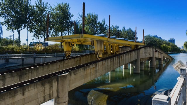 Yellow rail bridge over river in Beijing, with clear sky and urban greenery.