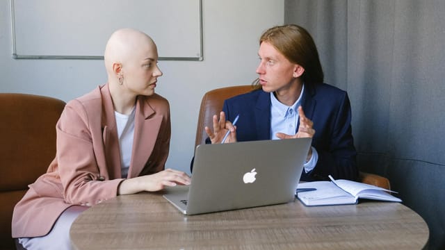 Two colleagues engaging in a focused business meeting with laptops and notebooks indoors.
