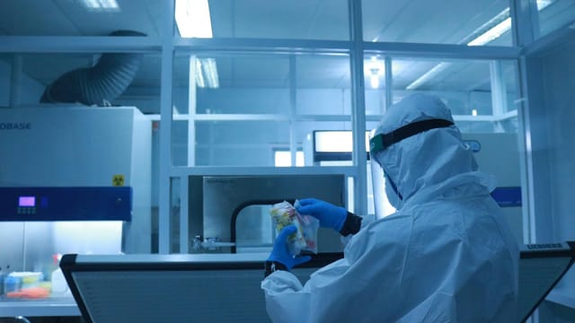 Lab technician in full protective suit performs tasks in a controlled laboratory environment.