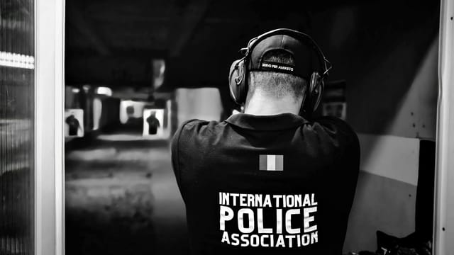 A police officer aiming at targets in an indoor shooting range, shot from behind in black and white.