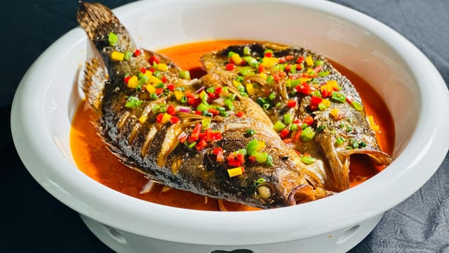 Traditional spicy fish dish served with colorful peppers in a white bowl.