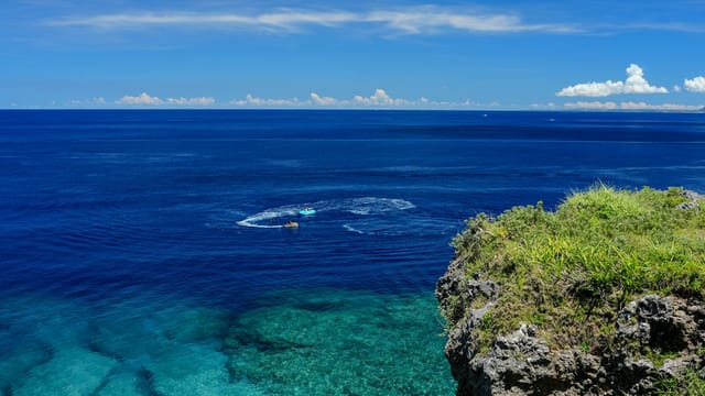 Breathtaking view from an Okinawa cliff overlooking the serene, crystal-clear sea under a vibrant blue sky.
