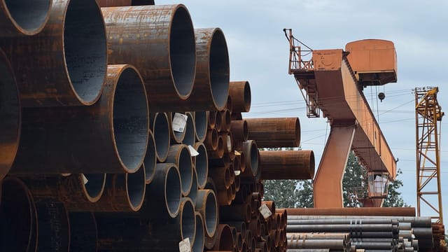 Stacked steel pipes beside an industrial crane in an outdoor yard, showcasing heavy industry and construction materials.