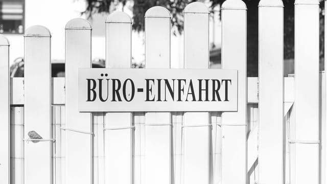 Black and white photo of an office entrance sign on a white picket fence with a tranquil setting.