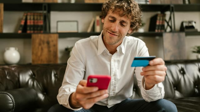 Caucasian man using smartphone and credit card for online shopping indoors.