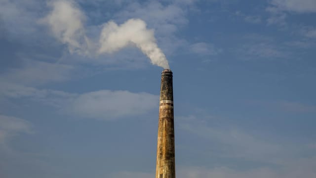 A factory chimney releasing smoke against a clear blue sky, highlighting air pollution.
